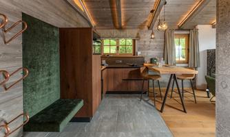 A modern kitchen with wooden details and a dining area. The walls are in a natural style, and large windows provide plenty of light.