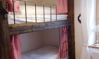 A cozy children's room with a wooden bunk bed. Red checkered fabrics and warm lighting create an inviting atmosphere.