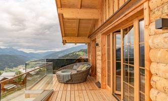 A cozy terrace with a round lounge chair. In the background, the mountains and a cloudy sky landscape can be seen.