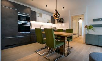 A modern kitchen unit with elegant, dark furniture and green chairs. The wooden steel table accommodates several people.