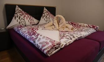 A cozy double bed with colorful bedding and decorative pillows. A wool blanket is artfully laid in the middle of the bed.