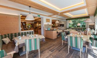 An inviting restaurant with bright wooden elements and a cozy atmosphere. The tables are tastefully set and there are green striped patterns on the chairs.