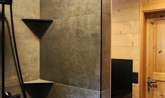 Modern shower with dark gray tiles and a large showerhead. In the background, there is a wooden shelf and a wooden door.