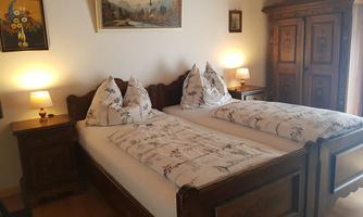 A cozy bedroom with two beds and decorative pillows. The walls are adorned with pictures, and there is a wooden dresser as well as bedside lamps.