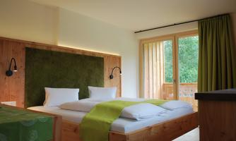 A modern room with a double bed and wooden details. Large windows provide plenty of daylight and a relaxed atmosphere.