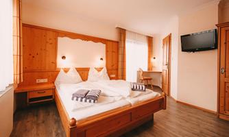 A cozy bedroom with a double bed and wooden paneling. The room is bright and has a television and a small workspace.