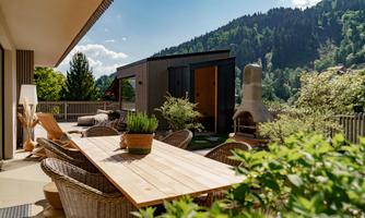 A stylish terrace with wooden furniture and a view of green mountains. The space is cozy and inviting, perfect for relaxing hours outdoors.