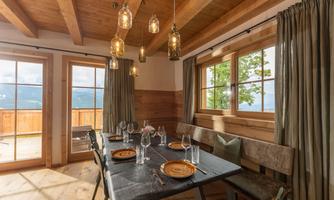 A cozy dining area with a large wooden table set for a feast. Large windows let in plenty of light and offer a beautiful view of the landscape.