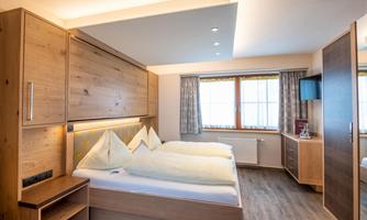 A modern bedroom with two beds and wooden paneling. Large windows provide plenty of daylight and a cozy atmosphere.