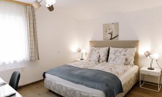 A bright bedroom with a large double bed and modern nightstands. The pleasant lighting and decorative curtains create an inviting atmosphere.