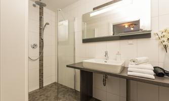 A modern bathroom with a shower and a sink. It is bright and clean, with white tiles and a minimalist design.