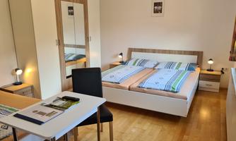 A cozy bedroom with a double bed and a desk. The room is bright and friendly, with wooden flooring and a mirror.