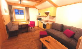 A cozy holiday apartment with a wooden ceiling. It has a sitting area, a dining table, and a modern kitchenette.