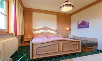 A cozy room with a double bed and a seating area. Warm wooden paneling and a friendly color shade create an inviting atmosphere.