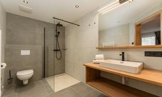 A modern bathroom with a large shower and an elegant wooden sink shelf. The walls are painted in neutral gray tones, creating a minimalist look.