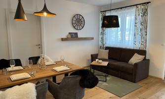 A modern dining room with a large wooden table and stylish chairs. A cozy sitting area with a sofa and beautiful decorations creates an inviting atmosphere.