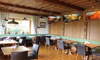 A cozy restaurant with wooden decor and bright light. Tables are set with black chairs and small flower arrangements.