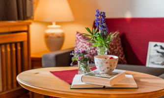 A cozy living space with a wooden coffee table. On the table, there is a book and a flower vase with colorful flowers.