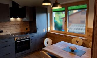 A modern kitchen with wooden paneling and a dining area. Large windows let in plenty of light and offer a view outside.
