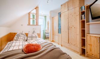 A cozy bedroom with wooden furniture and a large window. The decor is modern and inviting, featuring a bed and a television.