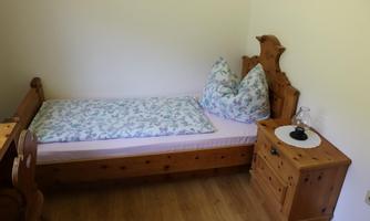 A simple room with a wooden bed and two pillows. Next to the bed is a small table with a lamp.