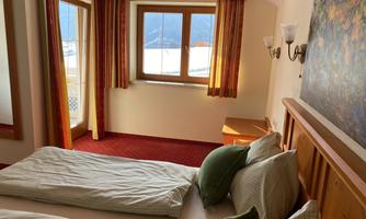 A cozy hotel room with two beds and a wooden detail. Large windows let in plenty of daylight and offer a view outside.