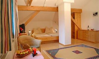 A cozy room with wooden beams, two beds, and a comfortable armchair. The space is bright and invites relaxation.