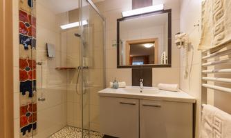 A modern bathroom with a glass shower and an elegant sink. The walls are brightly tiled, and there are towels and a hairdryer available.