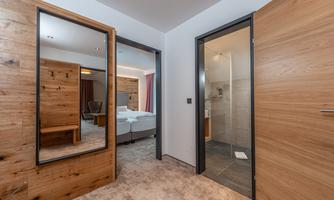 A modernly designed hotel room corridor with two doors and a large mirror. The space features bright walls and warm wood design.