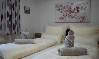 A cozy bedroom with two beds covered in beige bedding. On the beds are artistically folded towels.