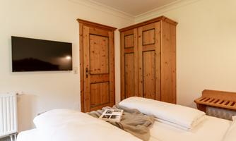A cozy bedroom with a double bed and a television on the wall. The decor is made of wood and conveys a warm atmosphere.