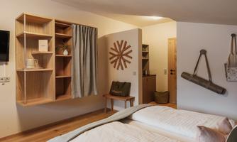 A modern room with two beds and a wooden shelf. Decorative elements like a wall clock and a curtain enhance the cozy atmosphere.