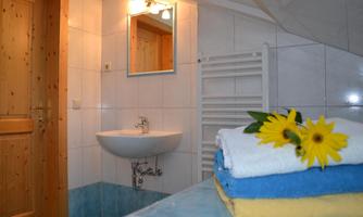 A modern bathroom with bright tiles and a sink. On a shelf, neatly folded towels and a sunflower serve as decoration.