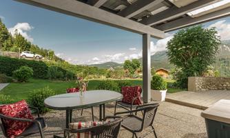 A cozy outdoor area with a table and chairs. In the background, green meadows and mountains can be seen.