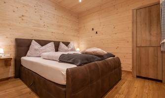 A cozy bedroom with a large bed and wooden paneling. The warm tones and soft lighting create a relaxed atmosphere.