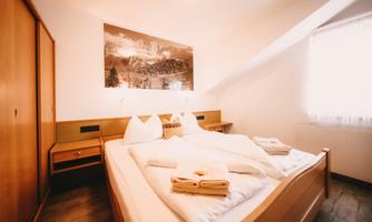 A cozy bedroom with a large bed and freshly washed towels. A beautiful picture of a mountain landscape hangs on the wall.