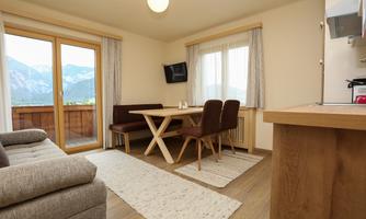 A bright, modern living and dining room with a view of the mountains. The furnishings include a sofa, a table and chairs, as well as large windows that let in plenty of daylight.