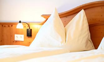 A cozy bedroom with a wooden bed frame and large pillows. Soft light creates a relaxed atmosphere.