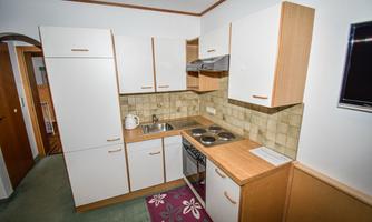 A modern kitchen with white cabinets and a bright, tiled floor. The equipment includes a sink, a stove, and a small countertop.