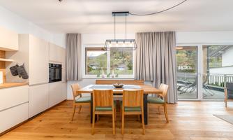 A modern dining area with a wooden table and several chairs. Large windows let in plenty of natural light and provide a view outside.