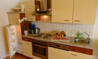 A modern kitchen with wood and cream color tones. It features a stove, a sink, and an open refrigerator door full of fresh food.