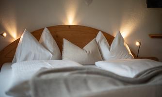 A cozy bed with several pillows and a soft blanket. Soft lighting creates a relaxed atmosphere in the bedroom.