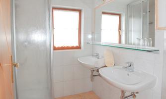 A modern bathroom with two sinks, a mirror, and a shower. The walls are brightly tiled and there is a window for daylight.