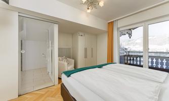 A modern bedroom with a large bed and a balcony. The room has plenty of light and an adjacent shower.