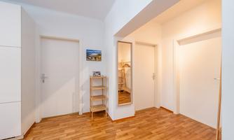 A bright hallway with wooden floors and white walls. There are several doors and a mirror.