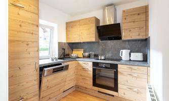 A modern kitchen with wooden cabinets and black countertops. It is well equipped with appliances such as a stove, microwave, and refrigerator.