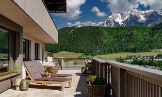 A beautiful balcony with loungers and a view of majestic mountains. The green landscape stretches to the horizon under a clear blue sky.
