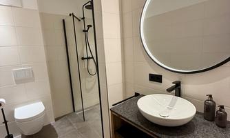 A modern bathroom with a shower, sink, and round mirror. The walls are brightly tiled, and the floor is covered with gray tiles.