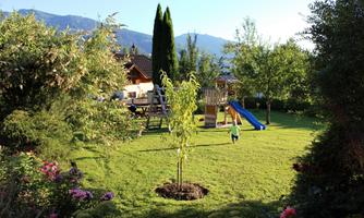 A beautiful garden with play equipment and a slide. In the background, there are trees and a blue sky.
