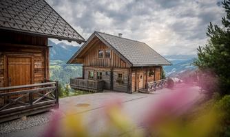 A picturesque mountain landscape with two wooden houses. The sky is cloudy and the surroundings feel calm and inviting.